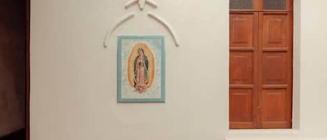 Um pátio com piso de azulejos, uma porta de madeira e um ícone religioso fixado na parede.