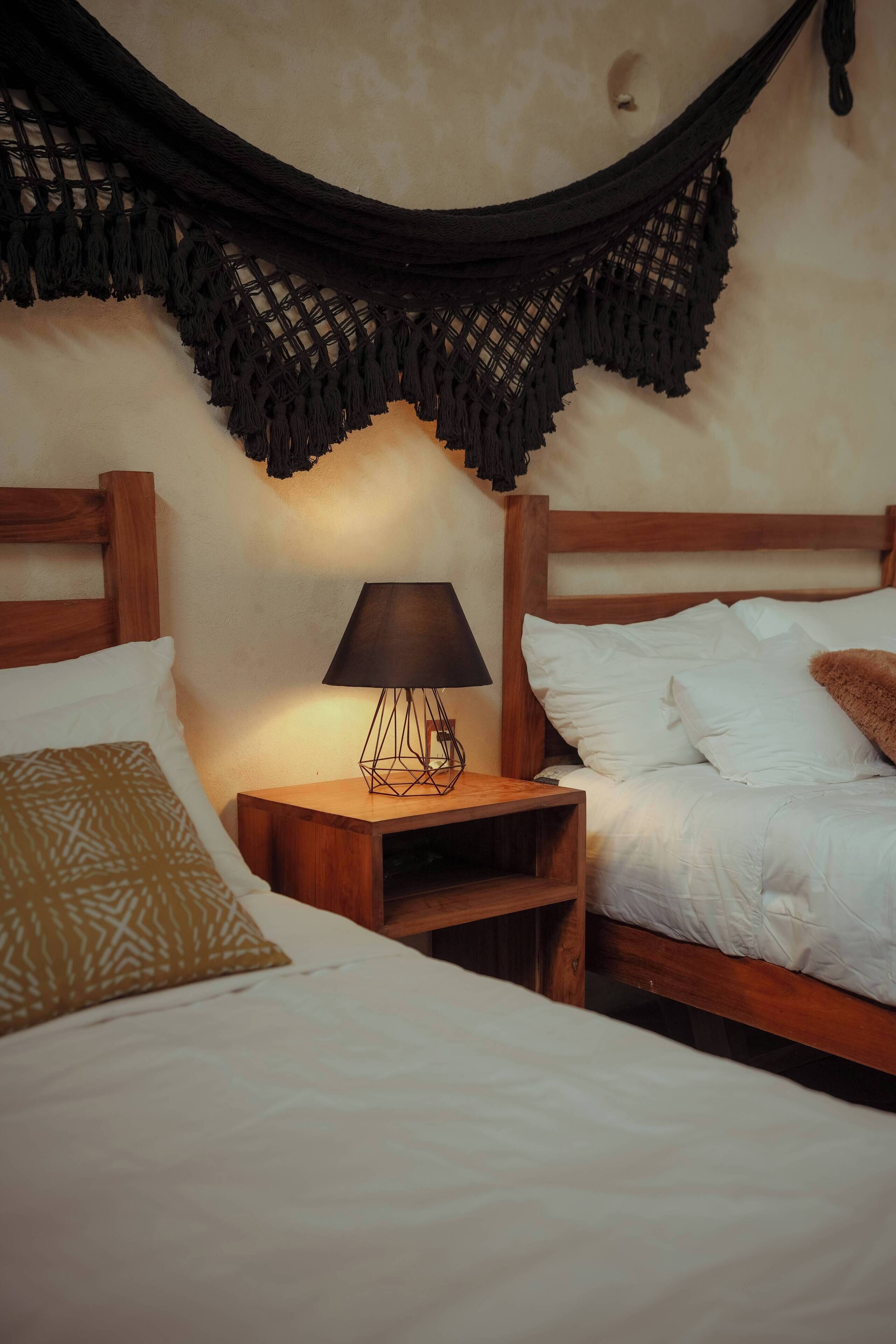 Un dormitorio con cabecera de madera, una mesita de noche con lámpara y una hamaca.