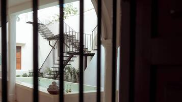 Blick durch ein vergittertes Fenster auf eine Treppe, die zu einer oberen Etage führt, mit gefliestem Boden und einem kleinen Außenbereich.