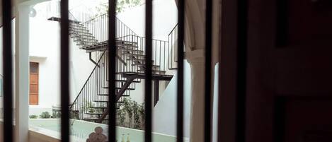 A view through a barred window of a staircase leading to an upper floor, with a tiled floor and a small outdoor area visible.