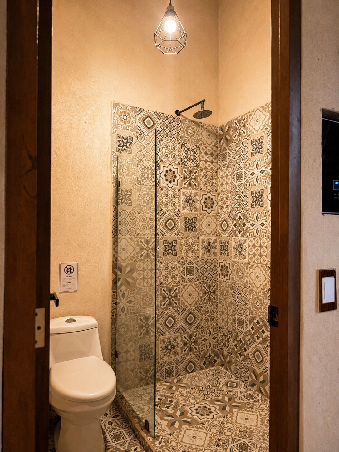 A bathroom with patterned tiles, a toilet, a shower with a glass door, and a hanging light fixture.