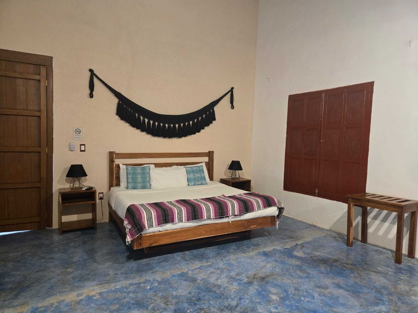 Un dormitorio con una cama de madera, dos mesitas de noche con lámparas, una hamaca y un gran puerta de madera.