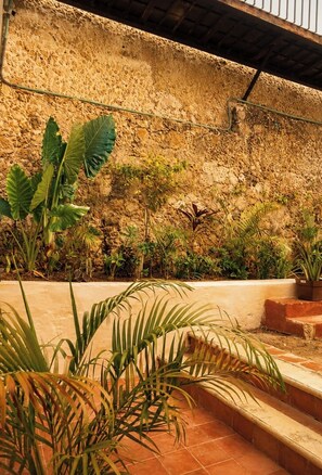 A stone wall with plants, a tiled floor, and steps leading up to a covered area. - Hotel Boutique Casa Jade (Campeche)