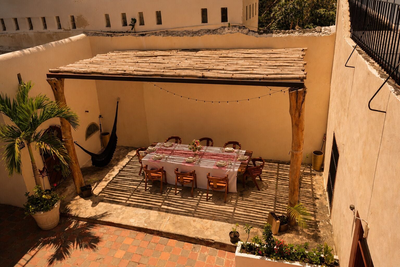 A covered outdoor dining area with a table set for four, surrounded by chairs, under a pergola.