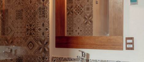 Un baño con baldosas estampadas, un espejo con marco de madera y un lavabo blanco.