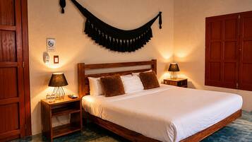 Habitación de hotel con una cama de madera, dos mesitas de noche con lámparas, una cortina negra colgada en la pared y un armario de madera.