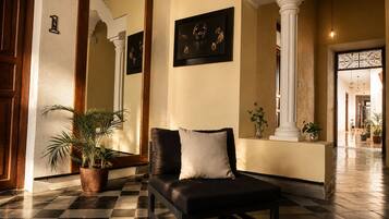 Un vestíbulo con piso a cuadros, un sofá de cuero negro con un cojín, un espejo grande y una planta en maceta.