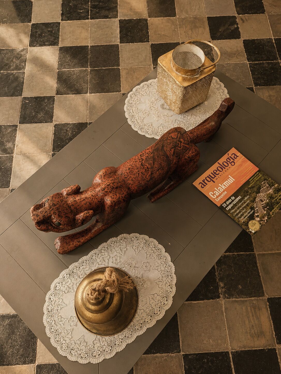 Ett bord med en dekorativ skulptur, en bok med titeln ”Arqueología” och en liten behållare.