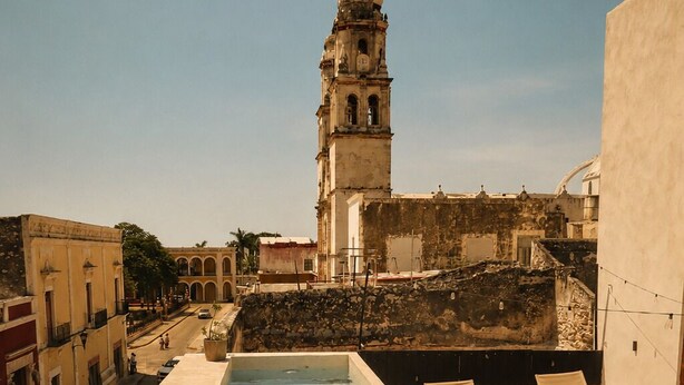 A swimming pool with a person in the water, a clock tower in the background, and a building with a balcony. - Hotel Boutique Casa Jade (Campeche)