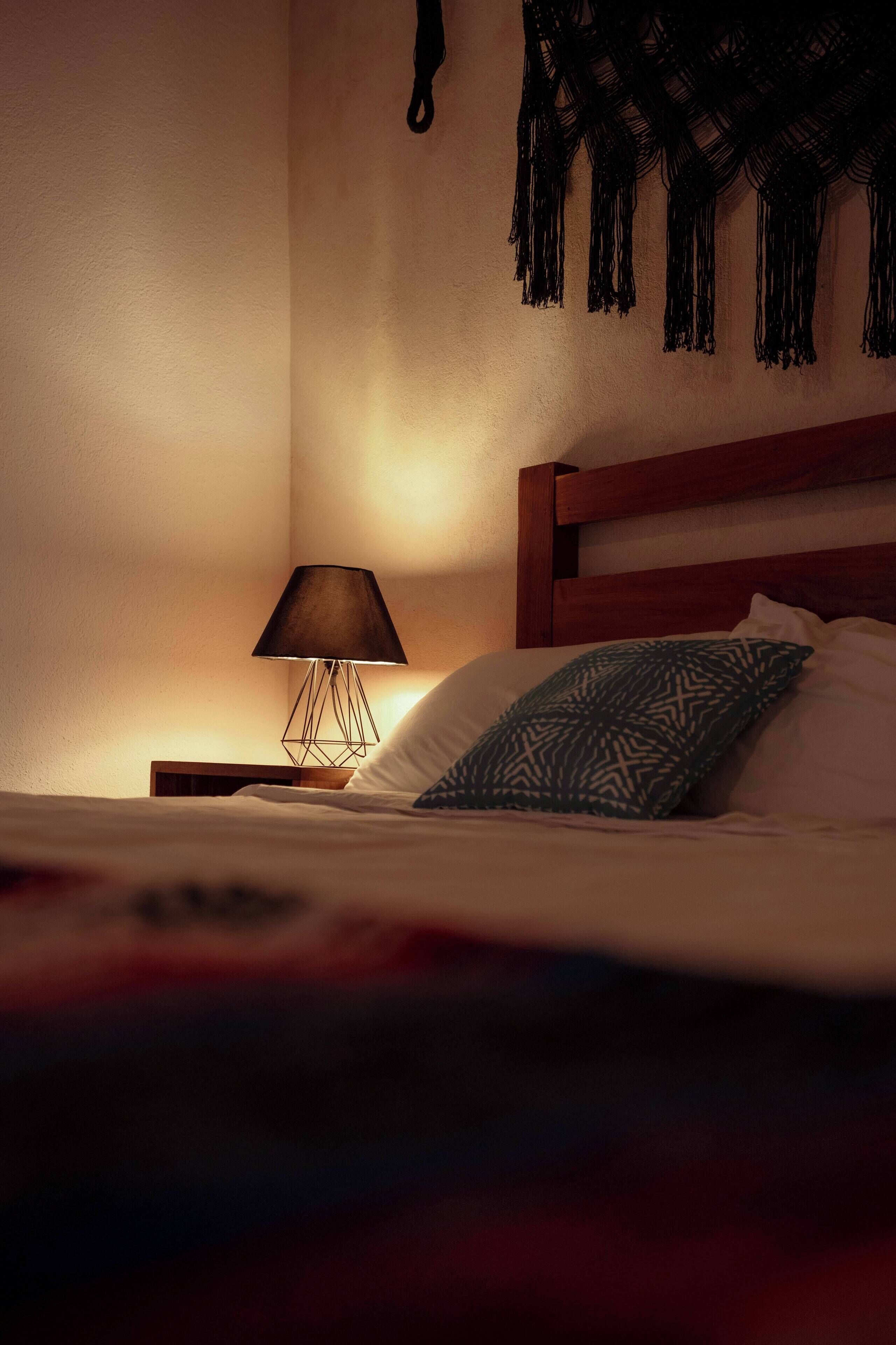 Cama bem arrumada com almofada estampada, abajur e um enfeite na parede.