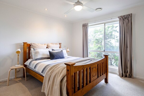A bedroom with a wooden bed, a nightstand, a lamp, and a window with curtains.