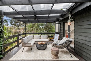 Relax on the outdoor patio with a sofa, armchairs, and coffee table, surrounded by a wooden railing and lush greenery.