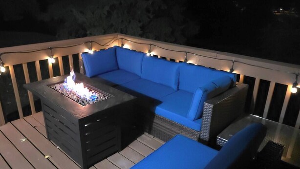 En udendørs terrasse med en indbygget pejseplads, en blå sofa og skammel.