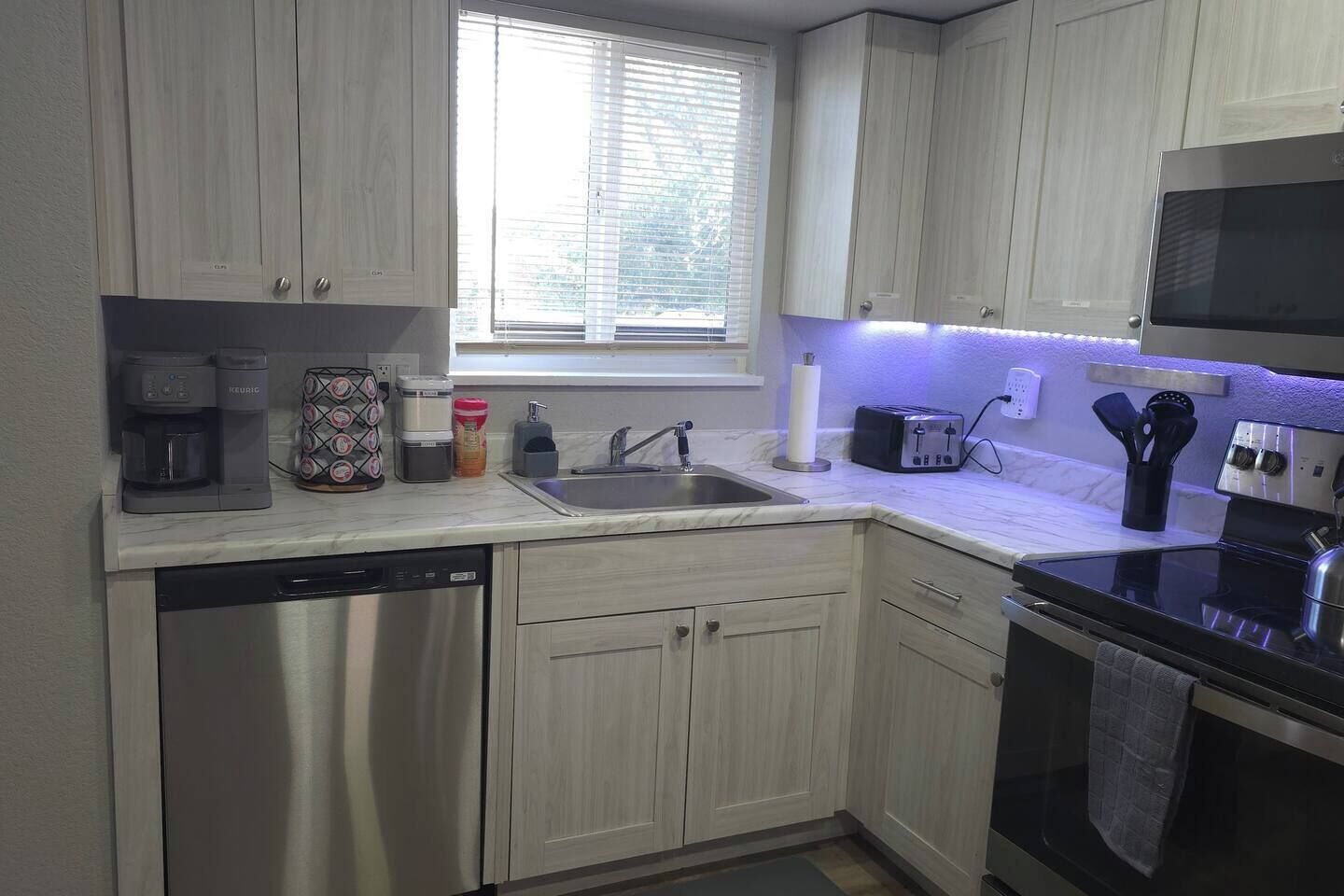 A compact kitchen with white cabinets, a dishwasher, a toaster, and a microwave.
