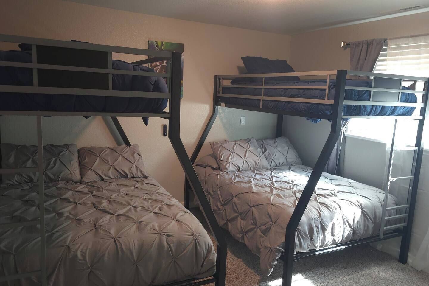 Ein Schlafsaalzimmer mit Etagenbetten, einem Fenster mit Vorhängen und einer Wandsteckdose.