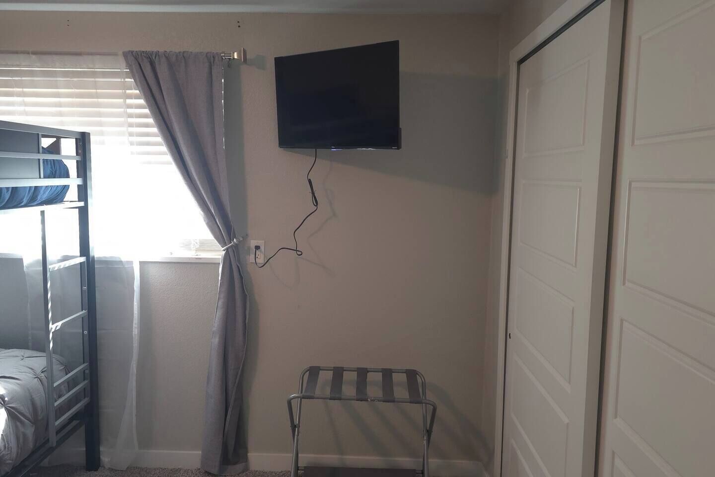 A room with a bunk bed, a TV mounted on the wall, a small table, and a door.