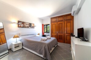Une chambre moderne avec un grand lit, une table de chevet avec une lampe, un téléviseur posé sur un meuble et une armoire.