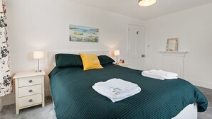 A neatly made bed with a green bedspread and white towels, a nightstand with a lamp, and a painting on the wall. - Delightful Family Getaway Cornwall (Falmouth)