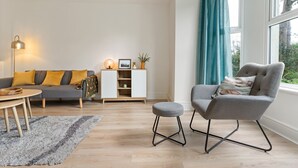 A modern living room with a grey sofa, a grey armchair, a small wooden table, and a white cabinet with shelves. - Delightful Family Getaway Cornwall (Falmouth)