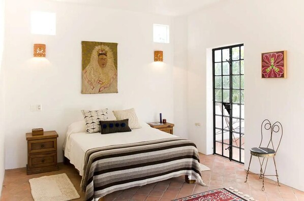 A bedroom with a bed, nightstands, a window, and artwork on the walls.