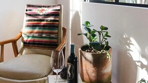 A cozy reading nook with a chair, a small table with a book and a bottle, and a potted plant.
