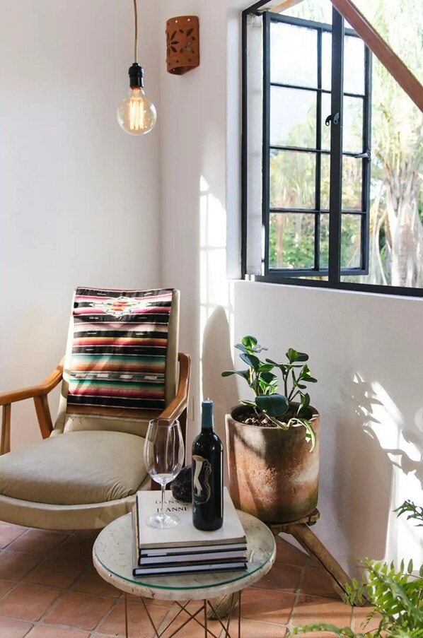 A cozy reading nook with a chair, a small table with a book and a bottle, and a potted plant.