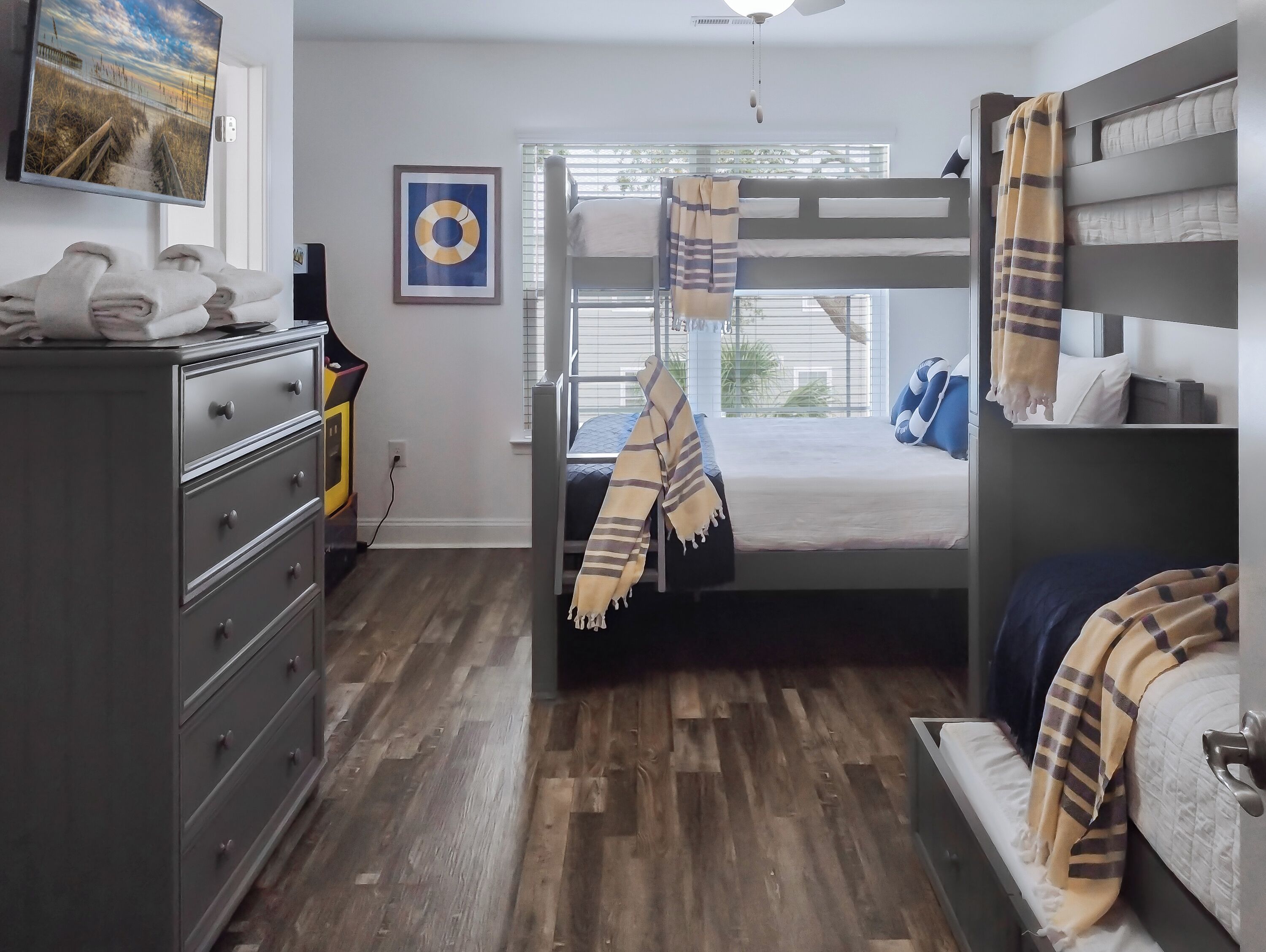 Una habitación con una cama litera, un escritorio con cajones, un televisor en la pared y una ventana con persianas.