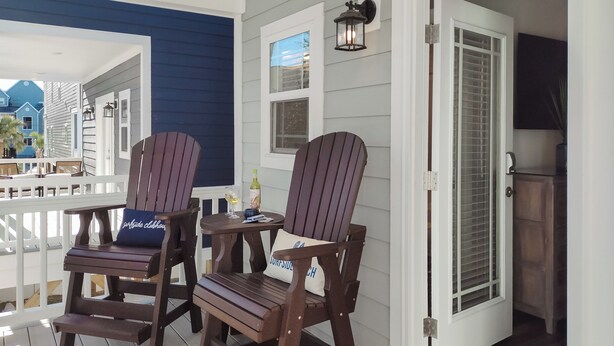A porch with two Adirondack chairs, a small table with a bottle and glass, and a door leading to an interior space. - Surfside Clubhouse: Steps to Beach & Heated Pool and Arcade Games! (Surfside Beach)