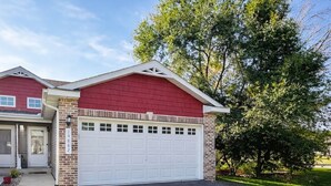 A two-story house with a red exterior, a white garage door, and a gravel driveway.