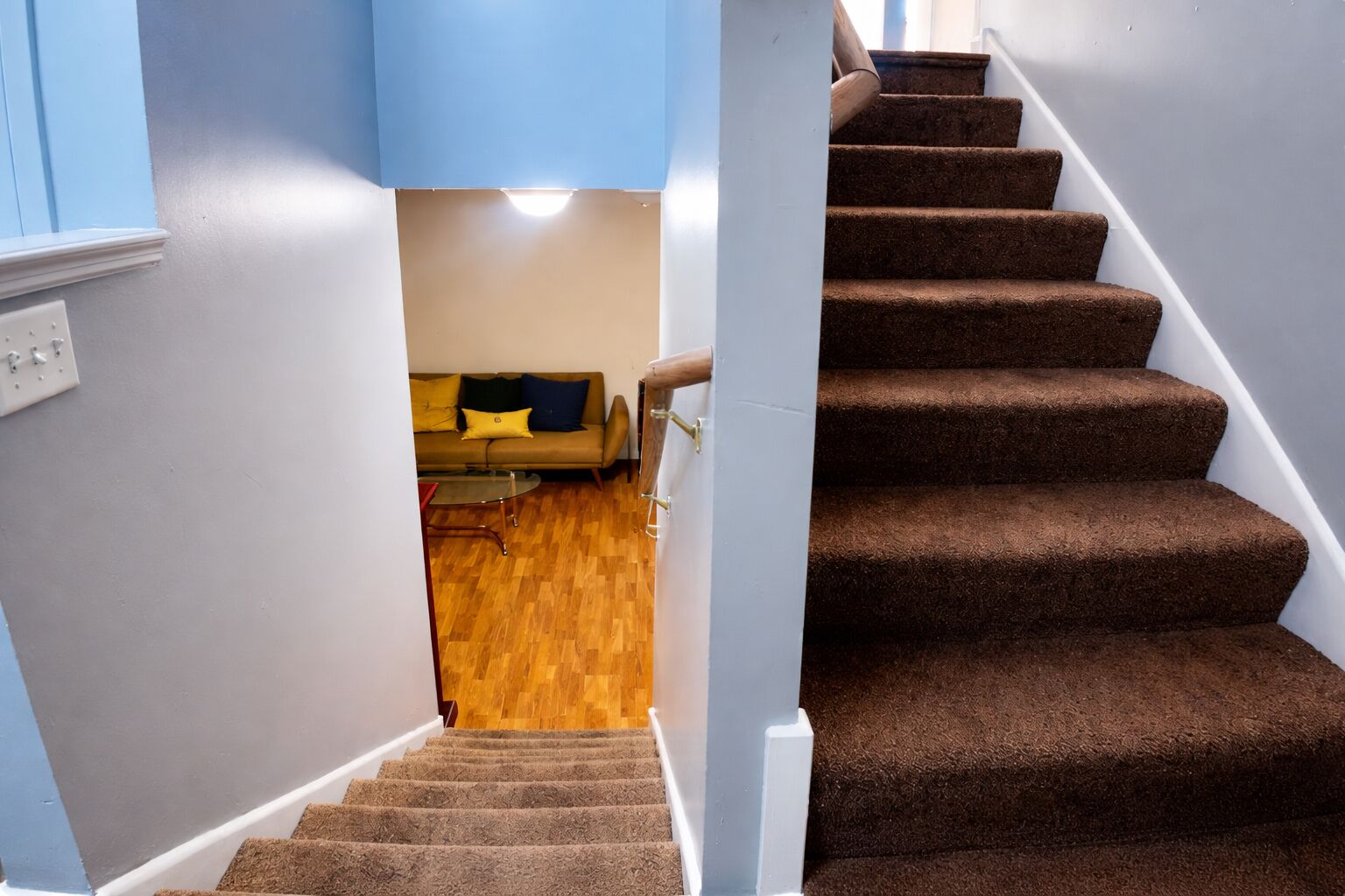 A staircase with carpeted steps leading to a room with a wooden floor and a sofa with cushions.