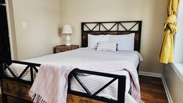Een net opgemaakt bed met houten frame, een bedlampje en een raam met gordijn.