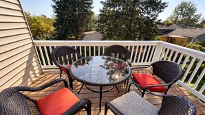 A deck with wicker chairs and a glass table, surrounded by a white railing.