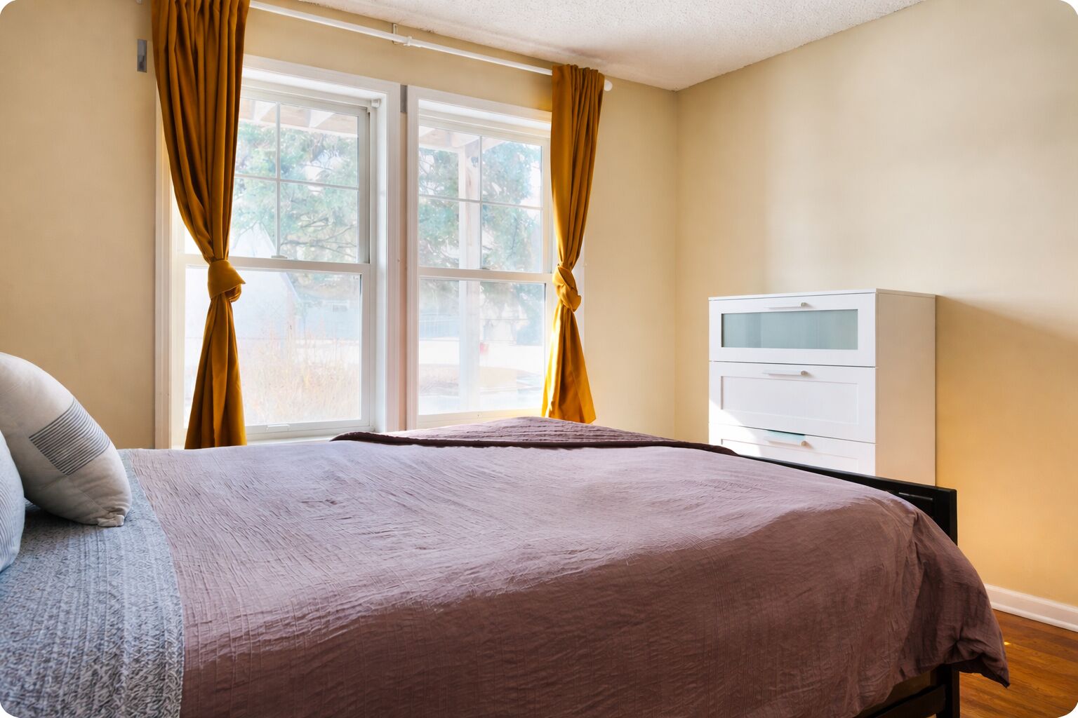 Ein Schlafzimmer mit einem Bett, einem Fernseher auf einem Schrank und einem Fenster mit Vorhängen.