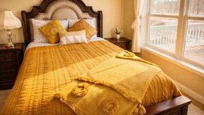 A bed with a yellow quilt, a wooden headboard, and a window with a view of a white fence.