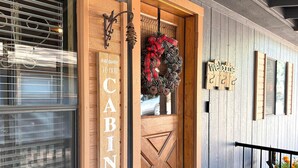 A wooden door with a 'Welcome to Cabin' sign, a decorative wreath, and a 'Welcome' sign on the wall. - Hardscrabble Mesa | Pine Trees | Wildlife | ADA (Pine)
