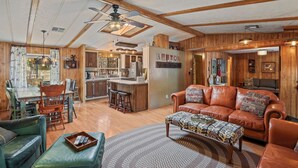 A spacious living area with a leather sofa, a dining table with chairs, and a kitchen in the background. - Hardscrabble Mesa | Pine Trees | Wildlife | ADA (Pine)