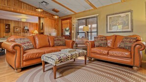 A cozy living room with leather sofas, a patterned ottoman, and wooden paneling on the walls. - Hardscrabble Mesa | Pine Trees | Wildlife | ADA (Pine)