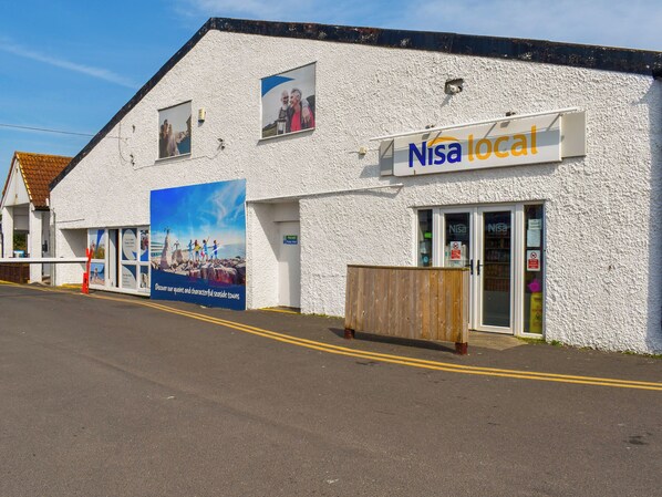 A building with a white exterior, a sign reading "Nisa local", and a large poster advertising seaside towns.