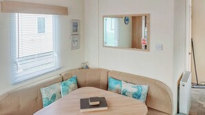 Un rincón acogedor con una mesa redonda, asientos mullidos, un espejo y una ventana con persianas.