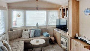 Una sala de estar acogedora con un sofá, una mesita redonda, un televisor y una zona de cocina con armarios y un microondas.