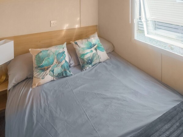 A bed with a light blue bedspread and two decorative pillows with a tropical leaf pattern.