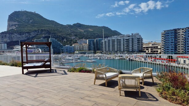 Una terrazza con mobili in vimini che si affaccia su un porto turistico e una montagna.