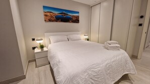 Un letto rifatto con un piumone bianco, una lampada da comodino e un asciugamano piegato a destra.