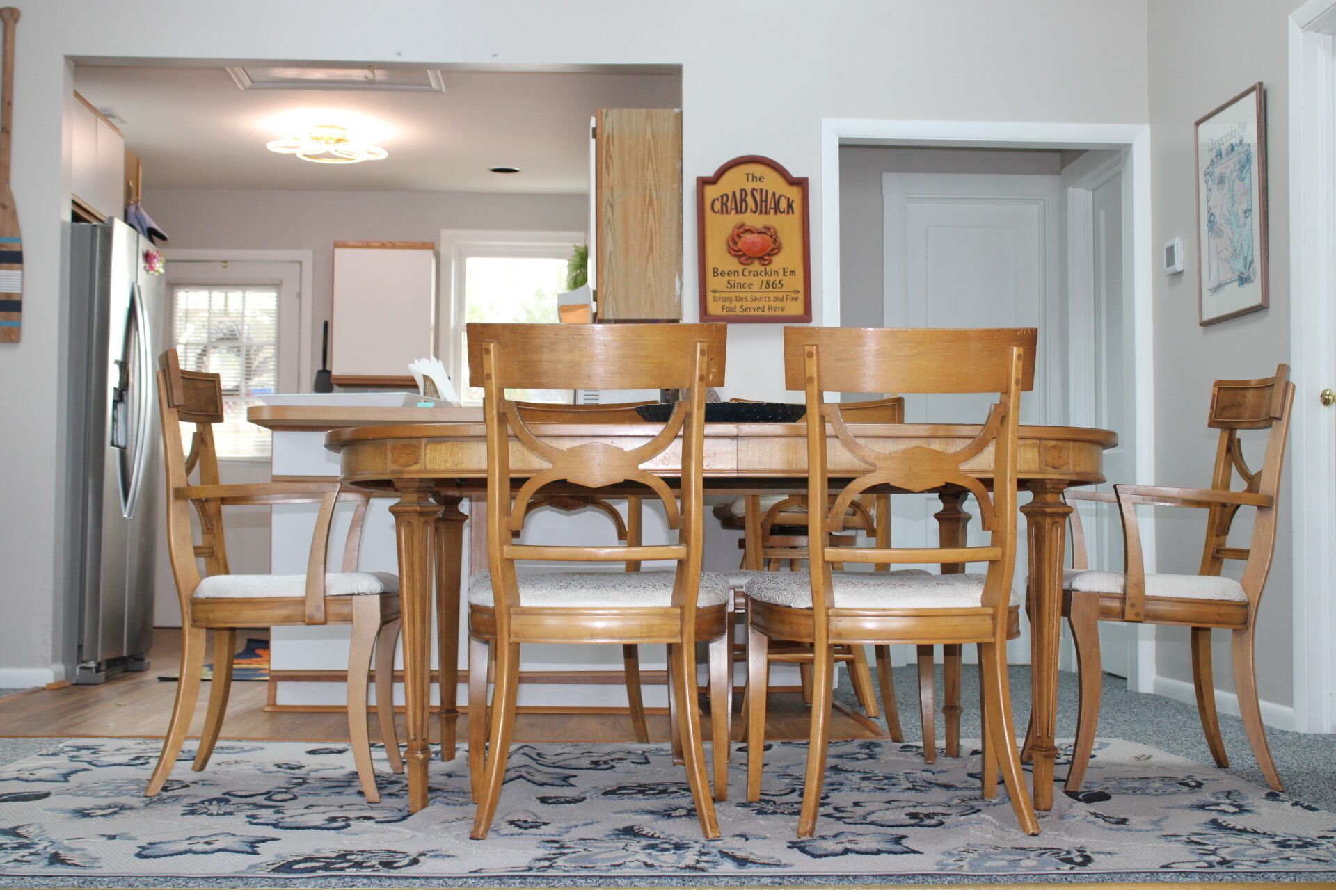 Un coin repas avec une table et des chaises en bois, un tapis et un panneau au-dessus de la table.
