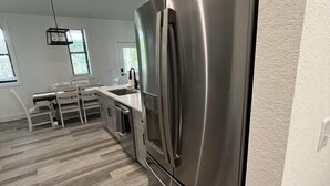 A modern kitchen with a stainless steel refrigerator, wooden flooring, and a dining area with white chairs. - The Rhododendron Cottage (Franklin)