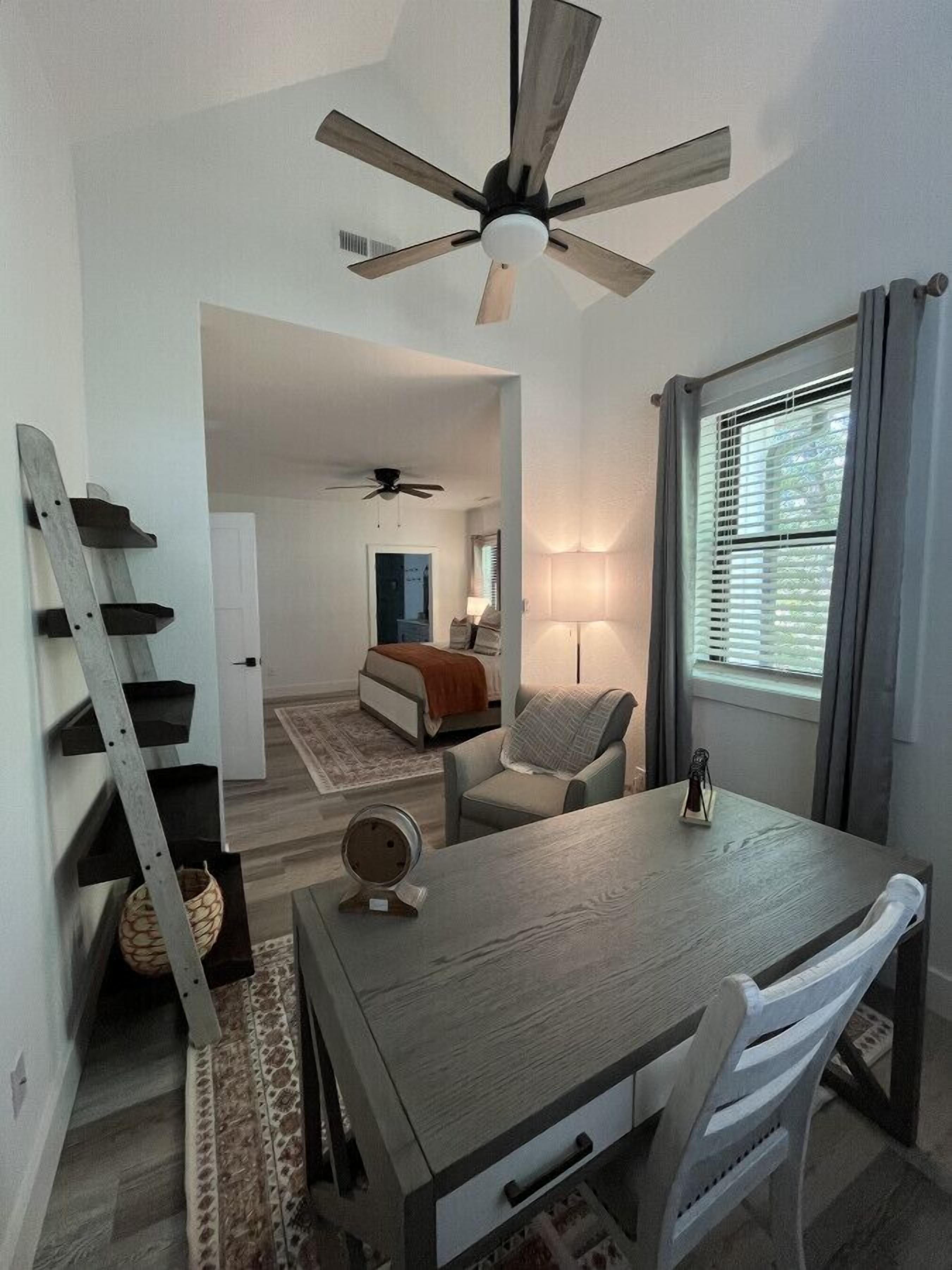 A compact room with a dining table, a chair, a ladder, and a ceiling fan.