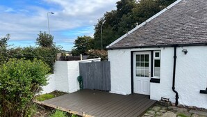 A small white cottage with a wooden deck, a grey fence, and a door with a window. - Cozy Gogarstone Cottage in Newbridge (Newbridge)