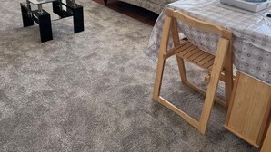 A living room with a grey carpet, a beige sofa, a glass coffee table, and a wooden side table. - Cozy Gogarstone Cottage in Newbridge (Newbridge)