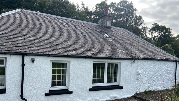 A white cottage with a grey tiled roof, two windows with white frames, and a stone pathway leading to the entrance. - Cozy Gogarstone Cottage in Newbridge (Newbridge)
