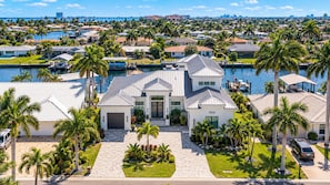 Une grande maison moderne avec un garage, entourée de palmiers et donnant sur une marina.